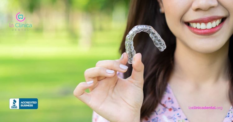 Mujer sonriendo y sosteniendo alineador Invisalign transparente en un entorno natural, destacando la innovación en tratamientos de ortodoncia estética en La Clínica Dental.