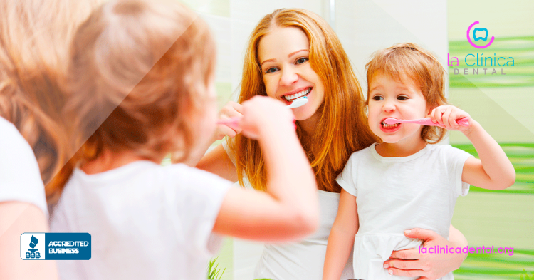 Mujer y niña cepillándose los dientes juntas, promoviendo la higiene dental familiar, con el logo de La Clínica Dental en la esquina superior derecha.