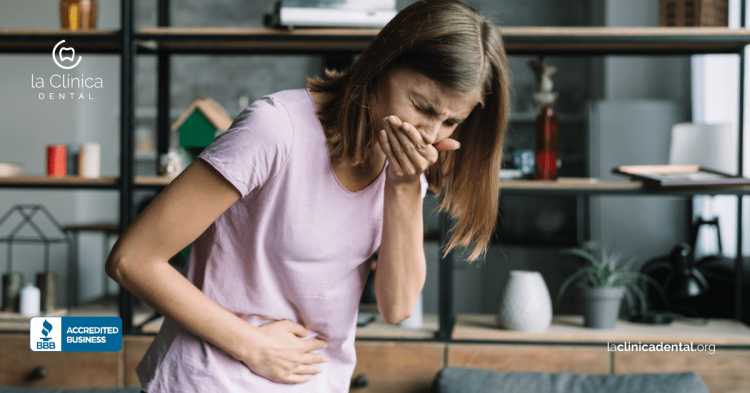 Mujer con malestar abdominal, tocándose el estómago, reflejando problemas estomacales relacionados con caries, con el logo de La Clínica Dental visible.