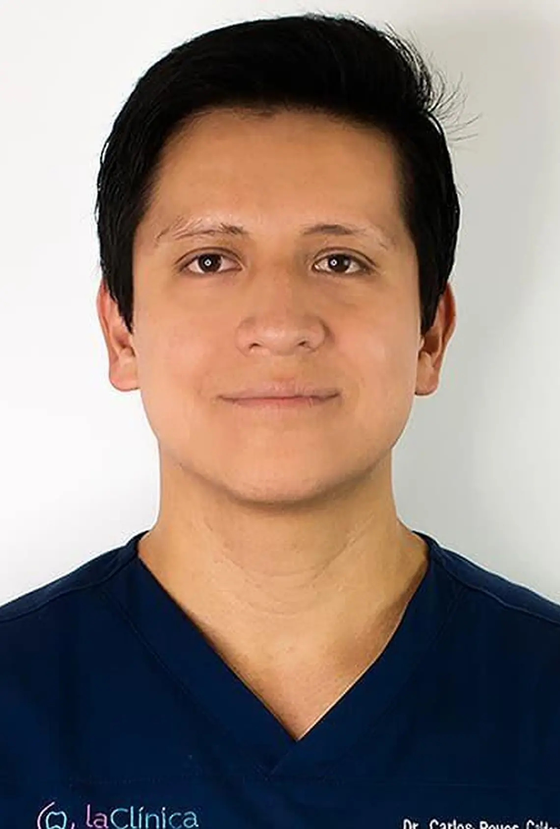 Dr. Carlos R. in dental scrubs, representing La Clínica Dental, smiling confidently against a neutral background, emphasizing his role in advanced dental care and treatments.