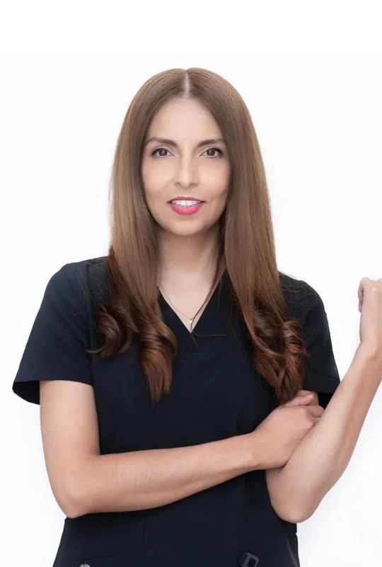 Mujer sonriente con cabello largo y lacio, vestida con uniforme dental negro, posando con los brazos cruzados, representando al equipo profesional de La Clínica Dental.