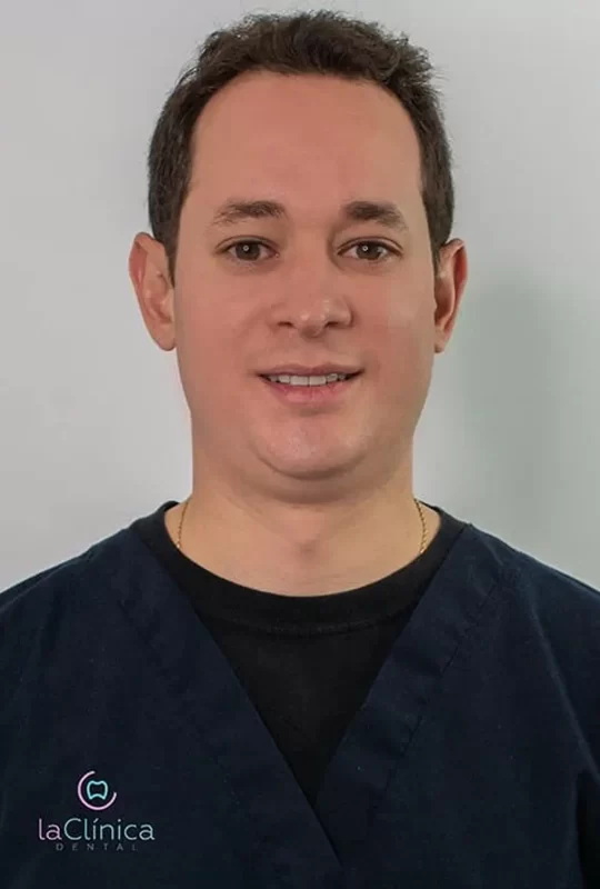 Médico dentista en uniforme, sonriendo, representando a La Clínica Dental, especializado en cirugía maxilofacial.