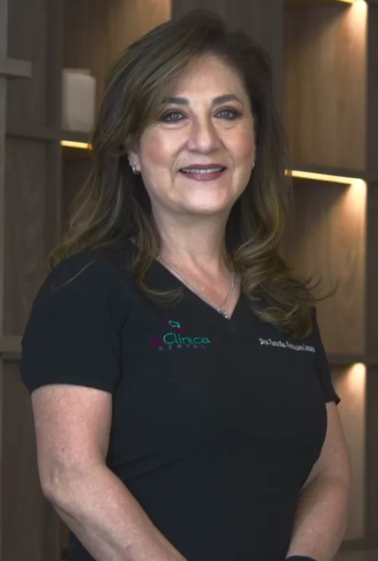 Dra. Hilda G., especialista en cirugía maxilofacial, con uniforme de La Clínica Dental, sonriendo en un ambiente moderno y profesional.