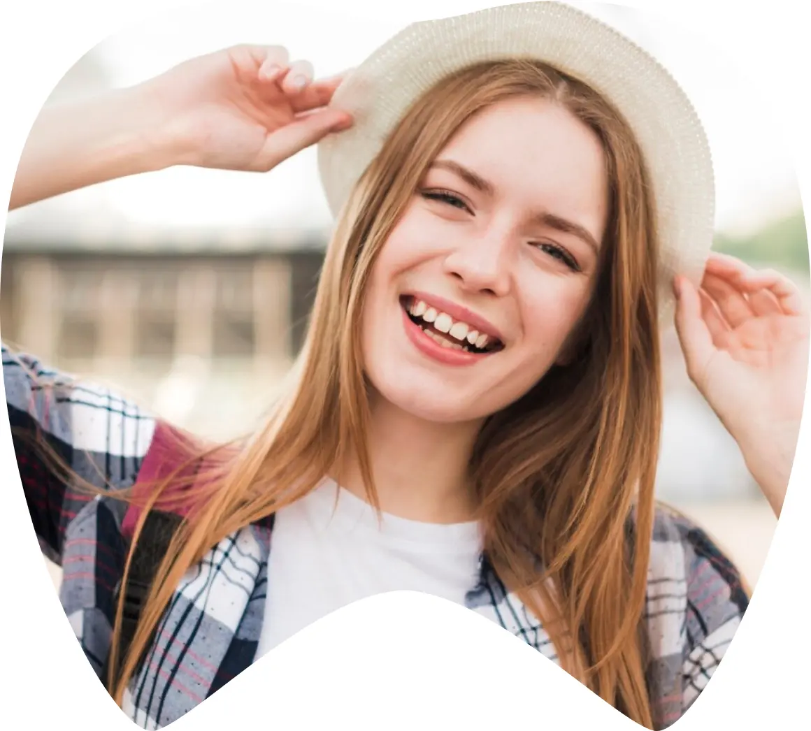 Mujer sonriendo y usando un sombrero, mostrando una sonrisa saludable, representando la confianza y la satisfacción tras un tratamiento dental.