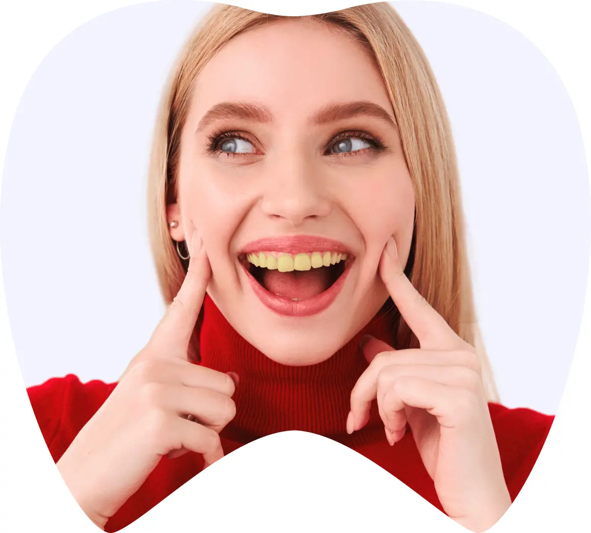 Mujer sonriente con dientes amarillos, mostrando su sonrisa y tocando su mejilla, simbolizando los resultados de tratamientos dentales en La Clínica Dental, enfocada en turismo dental en México.